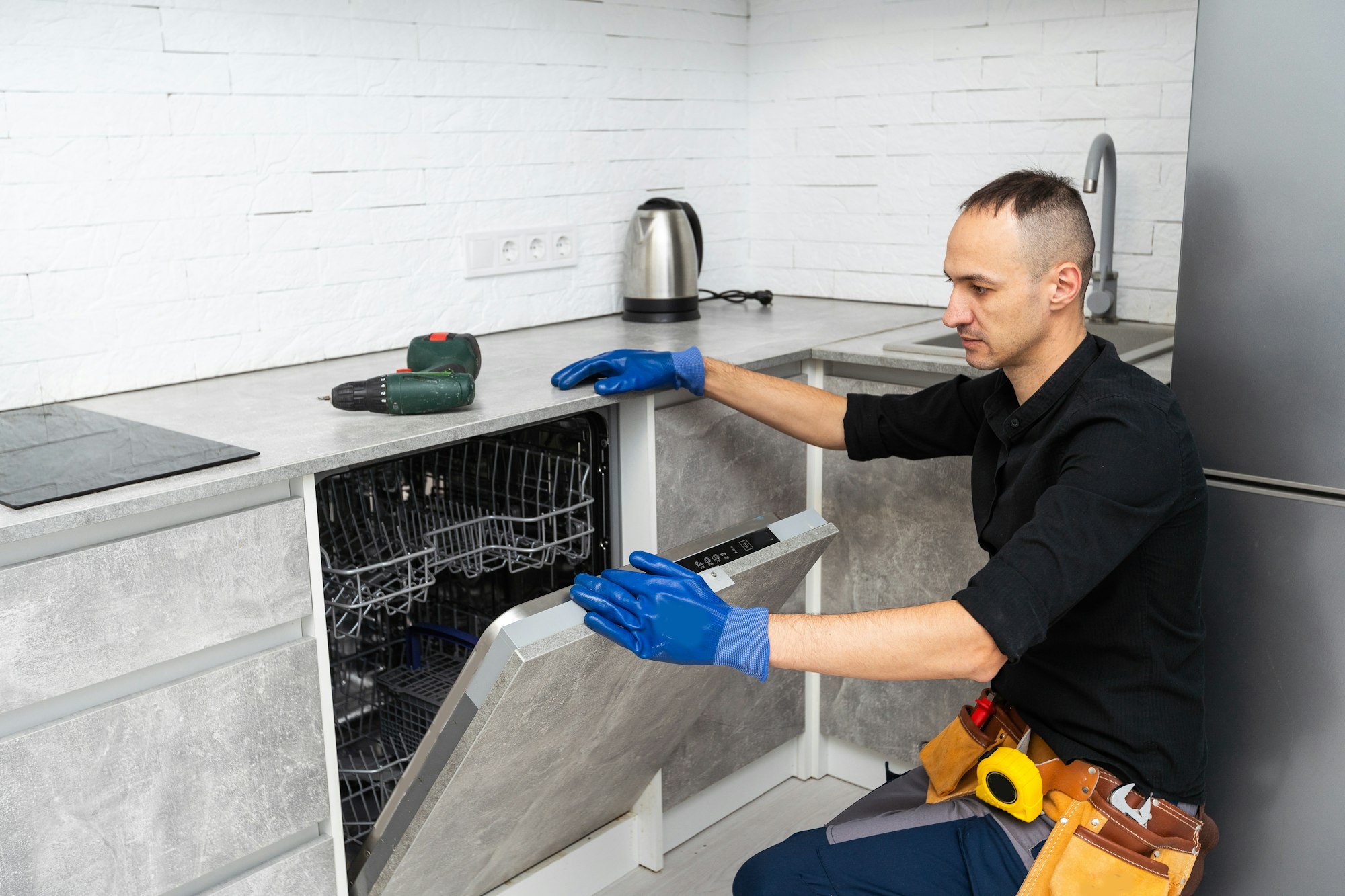 A plumber repairs a dishwasher in a kitchen room. Plumbing services.