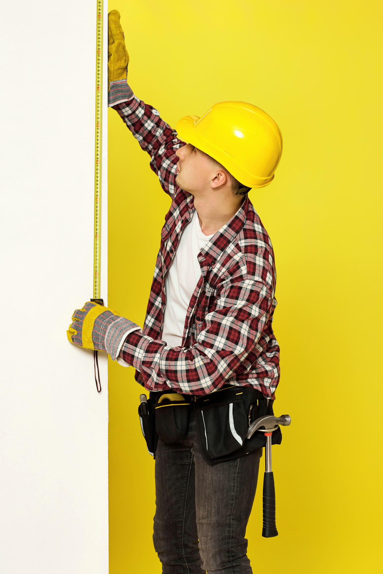 builder in work clothes, helmet taking measurements of wall