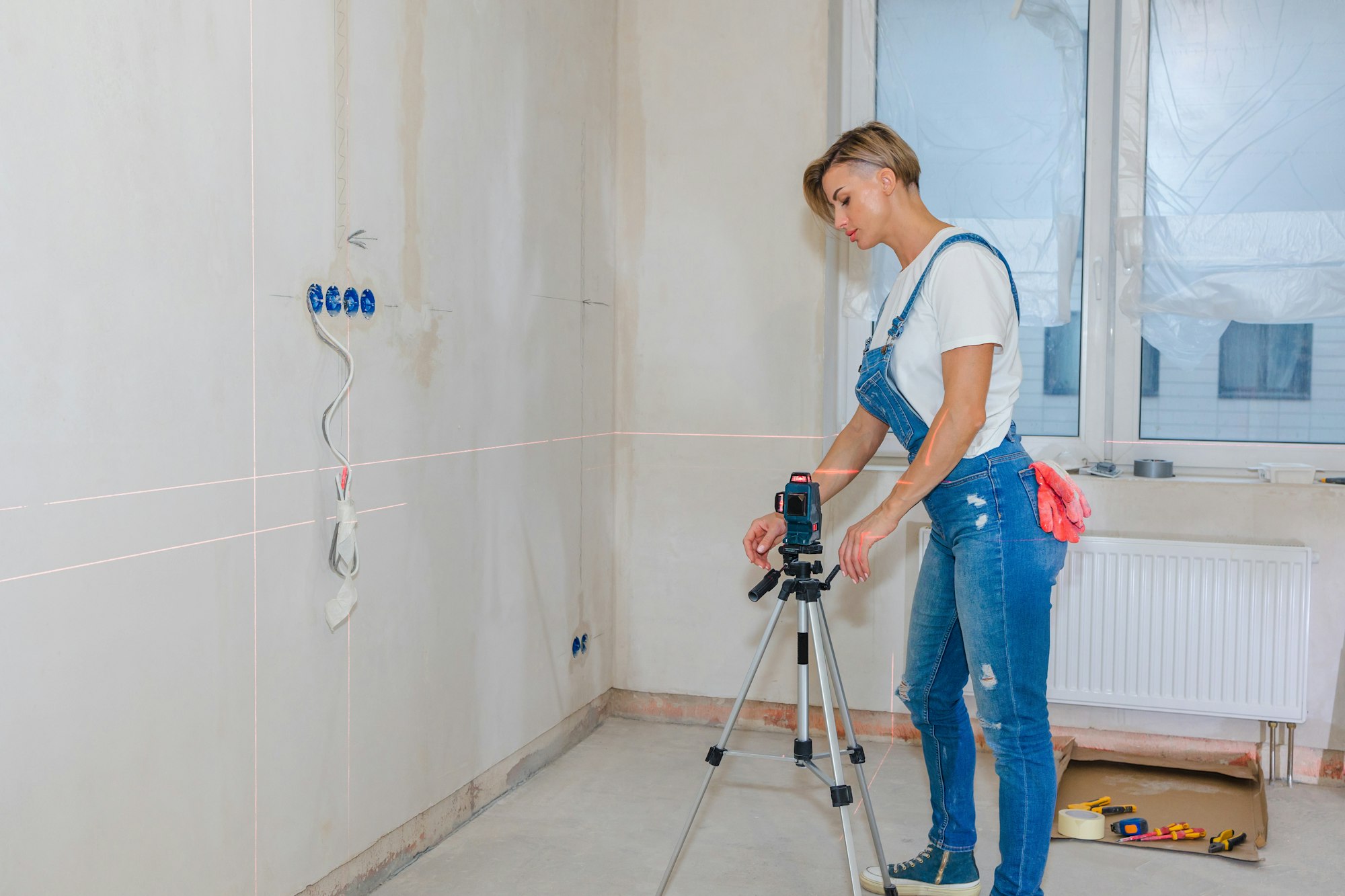 Woman makes repairs in new apartment. Builder levels walls using laser level